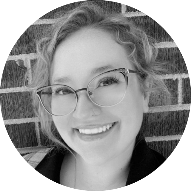 Smiling woman with glasses in front of a brick wall.