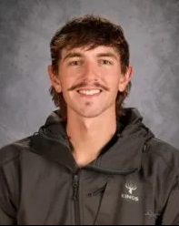 A man in a gray shirt is smiling for the camera.