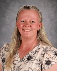 A woman with long blonde hair is smiling and wearing a green shirt.