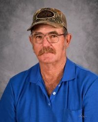 A man with a mustache and glasses is wearing a baseball cap and plaid shirt.