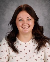 A woman with brown hair and a white shirt is smiling for the camera.