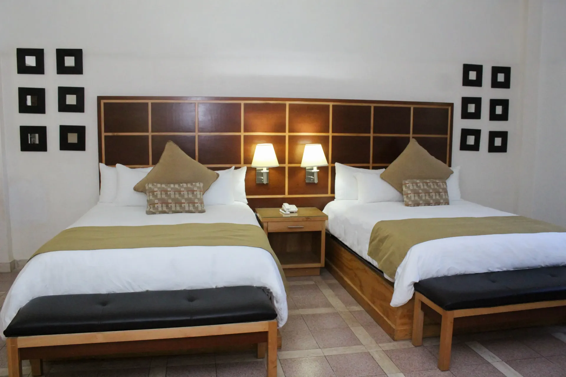Dos camas en una habitación de hotel con decoración dorada y marrón. Cada cama tiene un banco a los pies.
