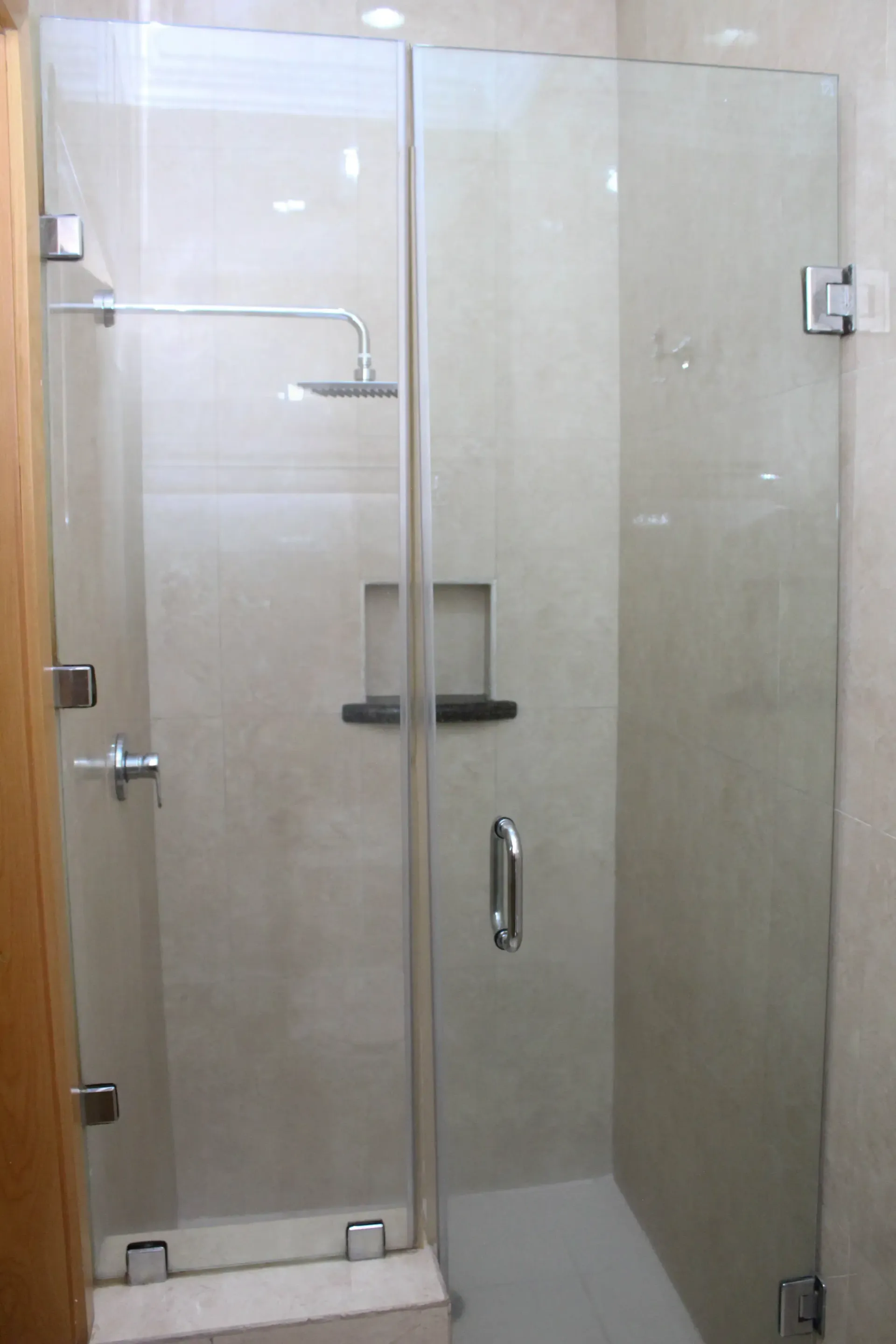 Cabina de ducha de cristal transparente con herrajes cromados en un baño alicatado.