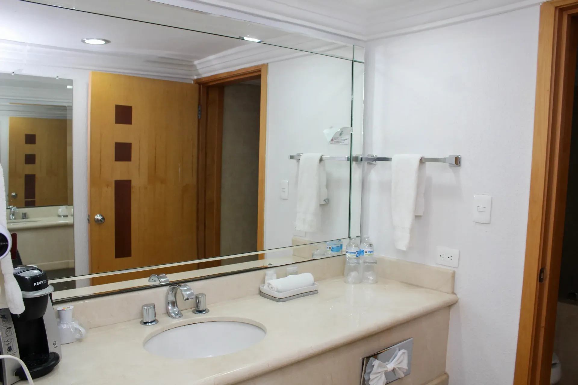 Baño con espejo, lavabo, toallas y puerta de madera cerrada.