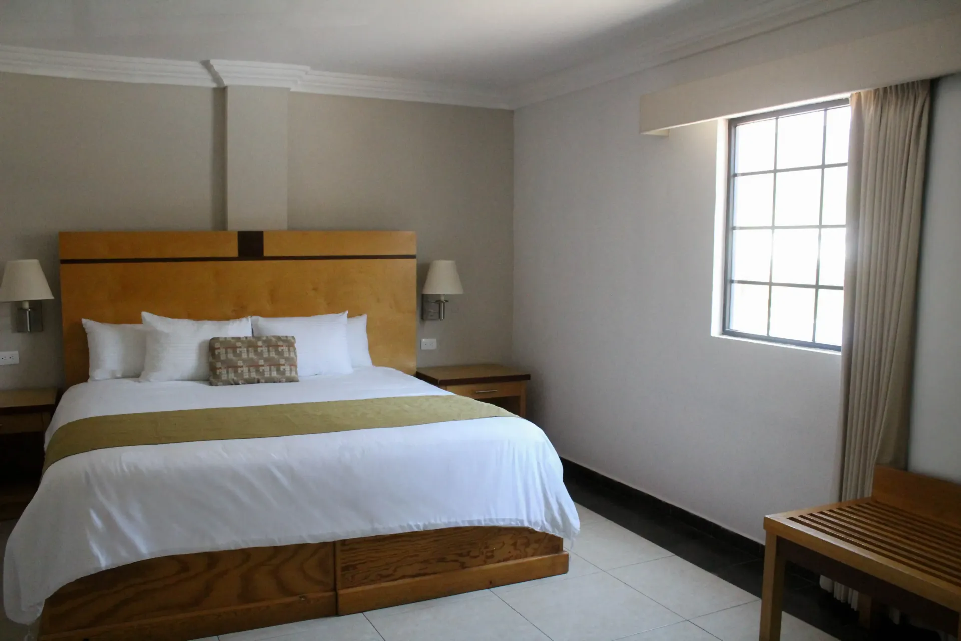 Dormitorio con cama grande, ventana y silla. Las paredes son de color neutro, la cama tiene sábanas blancas.