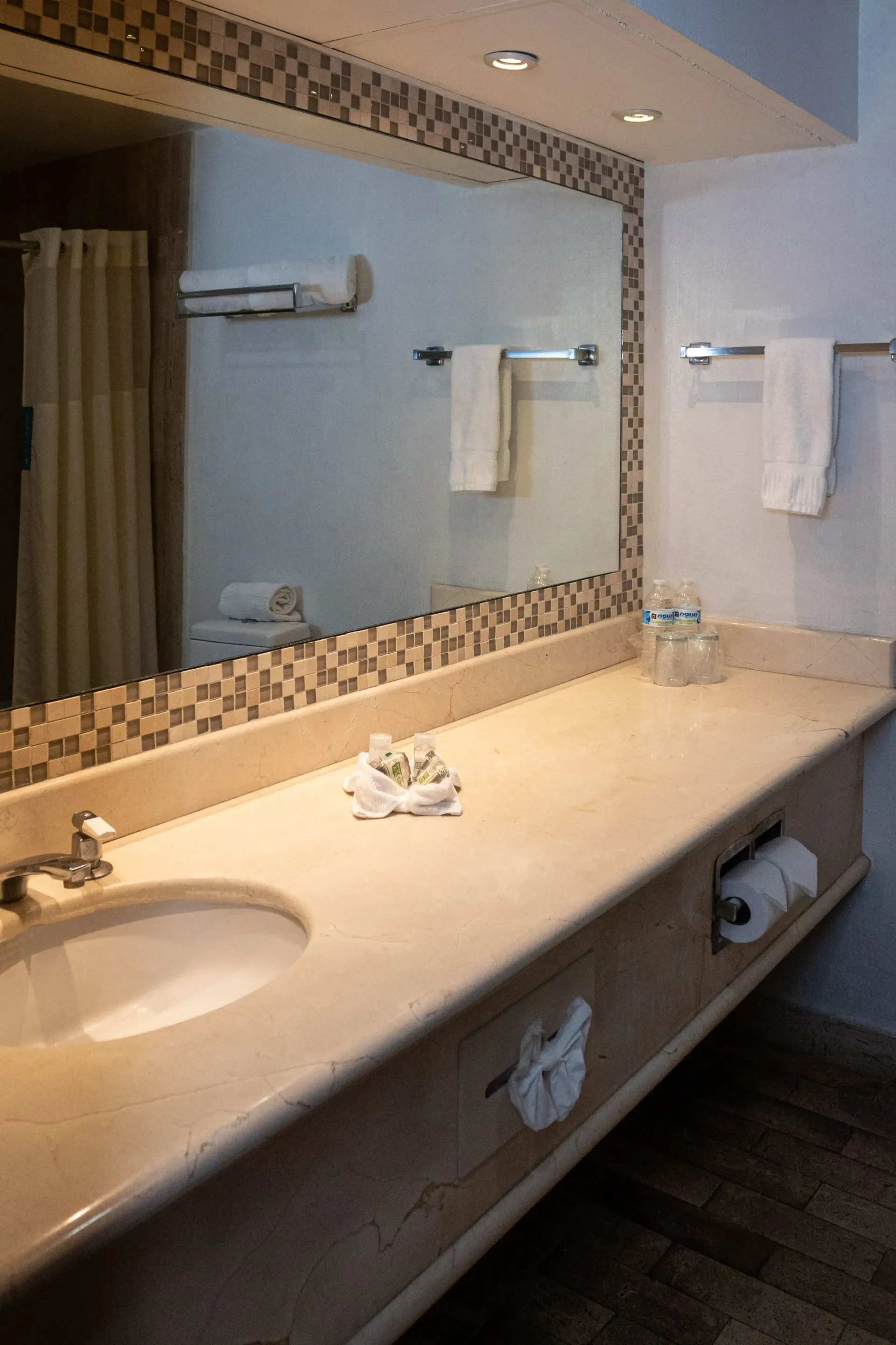 Tocador de baño con espejo grande, toallas y artículos de aseo.