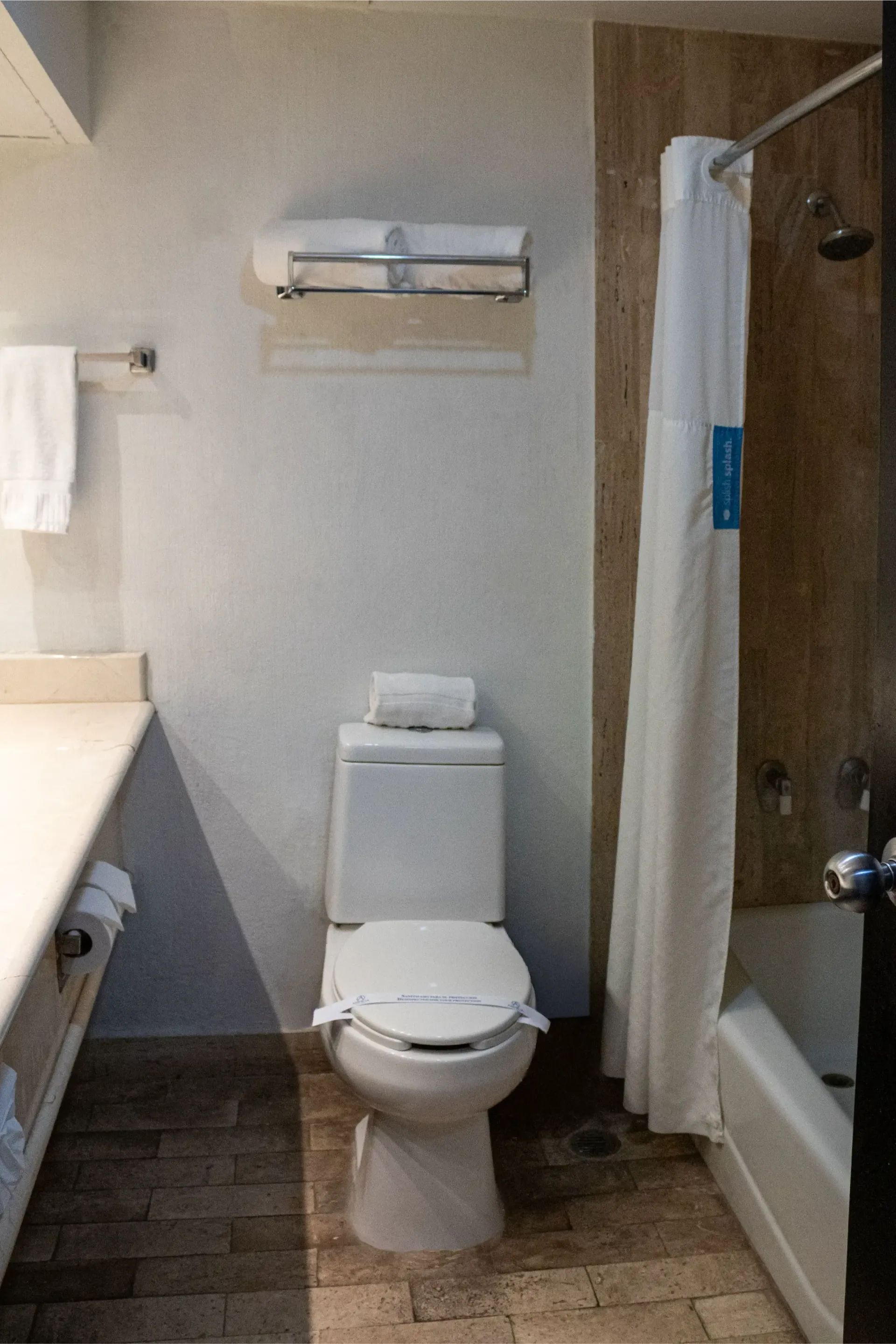 Baño con inodoro, ducha y lavabo. Paredes color beige, suelo de piedra.