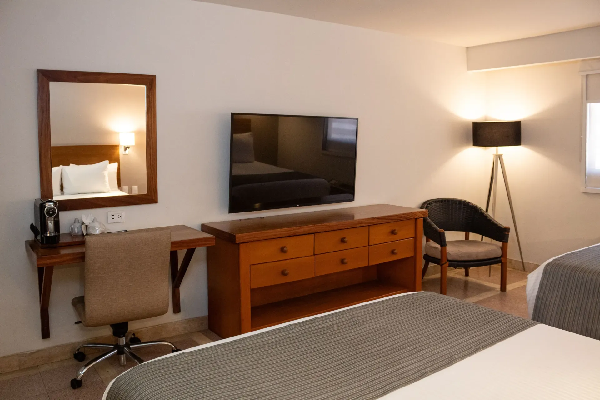 Habitación de hotel con dos camas, escritorio, televisor, cómoda, espejo y silla.