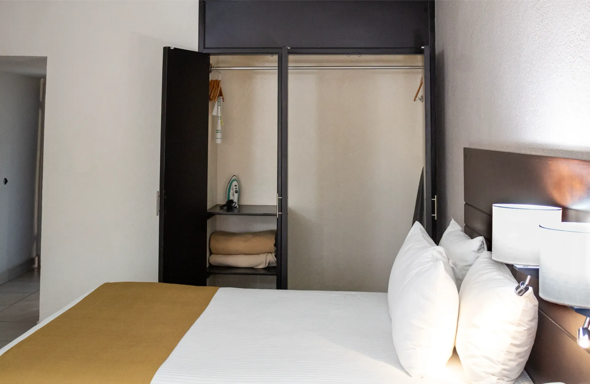 Dormitorio con armario abierto, ropa de cama blanca, cabecero marrón y pie de cama dorado.