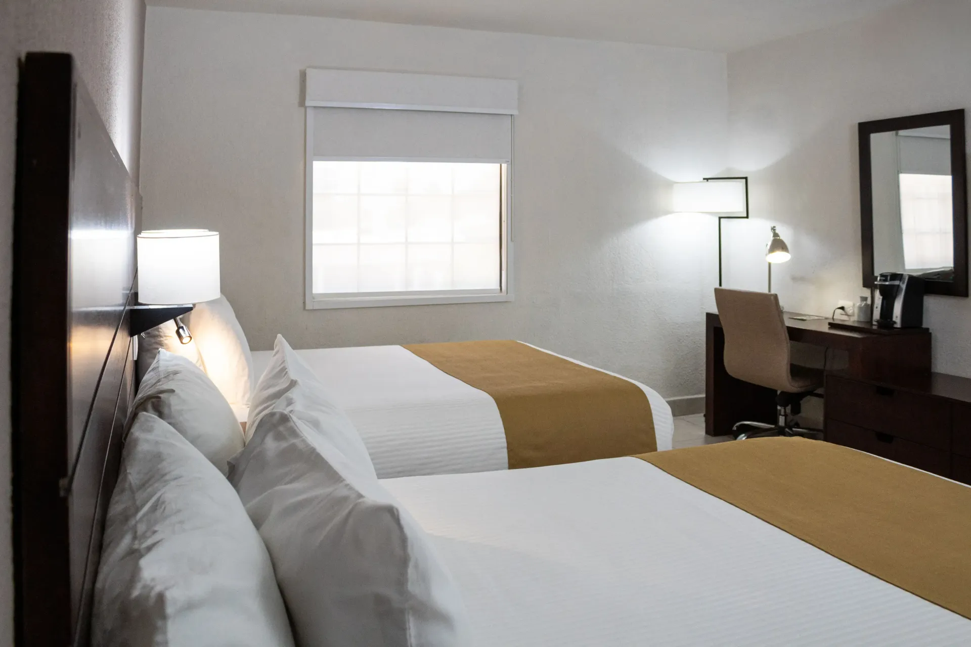 Habitación de hotel con dos camas queen, escritorio y ventana con persianas cerradas.