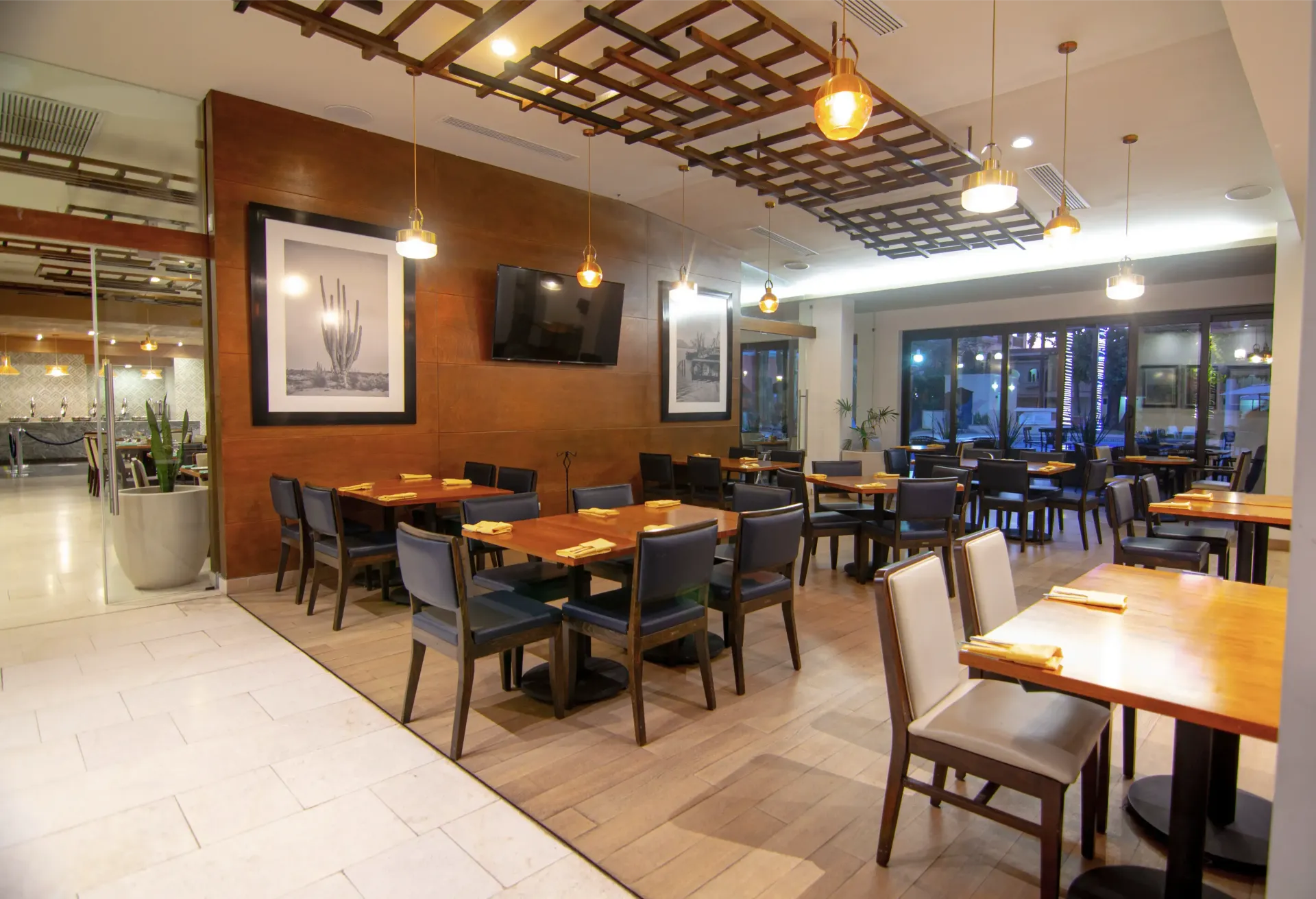 Comedor del restaurante con mesas cuadradas de madera, sillas oscuras, obras de arte y lámparas colgantes.