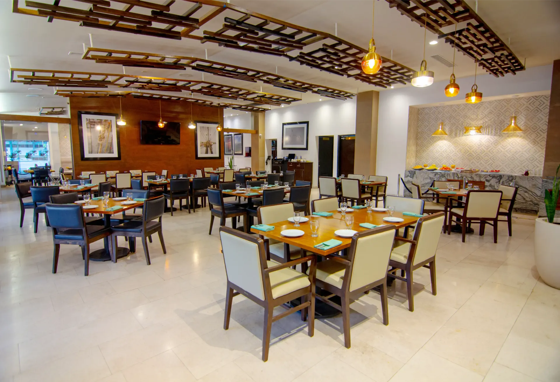 Comedor de restaurante con mesas, sillas y techo decorativo. Suelo y paredes de color claro, y bufé.