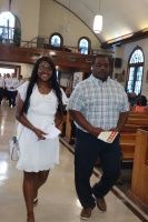 Two people walking down a church aisle, one in a white dress and one in a plaid shirt, smiling.