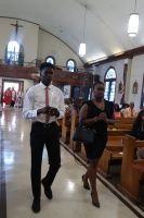 Two people walk down a church aisle, one holding a paper, with pews and arched windows in the background