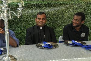 Two men seated at a decorated table, smiling during an outdoor event.