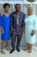 Three adults posing together indoors, wearing blue, navy, and light blue outfits.
