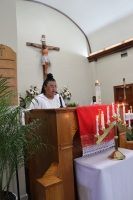 Priest speaking at a church lectern beside a red altar cloth and lit candles