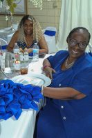 Two women seated at a table with a blue gift bag and decorations, smiling in a bright indoor room