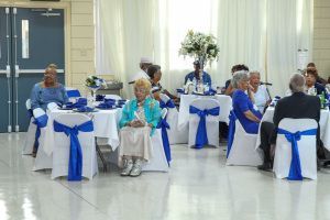 Guests seated at round tables with blue chair sashes in a bright banquet hall