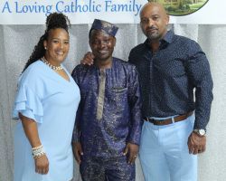 Three people posing indoors before a banner reading “A Loving Catholic Family.”