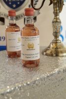 Two small clear bottles with amber liquid on a glittery table beside a gold candlestick.