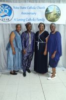 Four people pose indoors in front of a church anniversary banner, wearing formal attire.
