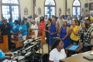 Congregants standing and clapping in a church sanctuary during a service, with a drum kit in the foreground