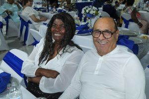 Two people smiling at a banquet table with white and blue chair covers in the background