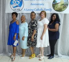 Five women posing in front of an “85th Anniversary” banner at a Catholic family event.