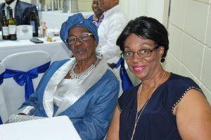 Two women seated at a banquet table, smiling in formal attire with blue and white decor.