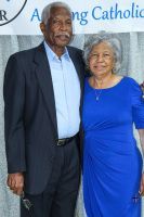 Two people posing together at an event, with a blue backdrop and a partly visible logo behind them.
