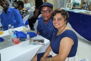 Two people smiling at a table in a banquet hall, with blue napkins and drinks nearby.