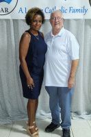 Two people posing together at a formal event, standing before a white backdrop with a logo.