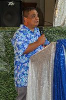 Man speaking into a microphone beside a blue-and-silver draped podium indoors