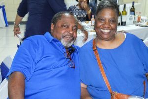 Two smiling people in blue shirts seated together at a table indoors
