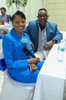 Two people smiling at a table in a bright indoor event setting, one in a blue outfit