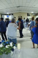 People standing and mingling in a bright indoor hall during a gathering, with floral arrangements in the foreground.