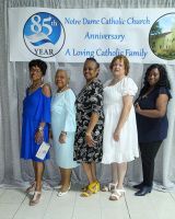 Five adults posing at Notre Dame Catholic Church anniversary event in front of a banner.