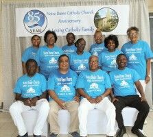 Group portrait of people in blue shirts at a church anniversary event, seated and standing before a banner