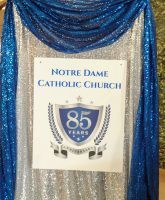 Notre Dame Catholic Church 85th anniversary sign with blue and silver draped backdrop