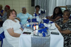 Five people seated at a decorated banquet table with blue and silver centerpieces, smiling indoors.