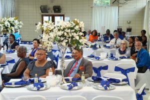Guests seated at decorated banquet tables in a bright event hall with blue-and-white table settings