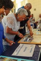People browsing items on a table at an indoor event, examining framed artwork and papers