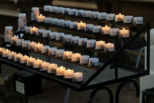 Rows of lit candles on a black metal stand in a dim indoor setting