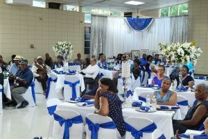 Banquet hall with guests seated at white tables decorated with blue bows and white flowers