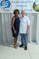 Two people posing in front of a Notre Dame Catholic Church anniversary banner.