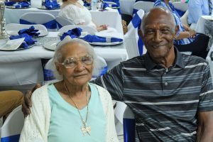 Two smiling people seated at a banquet table with blue-and-white decorations in the background