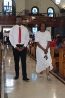 Two people standing in a church aisle during a ceremony, one in a red tie and one in a white dress.