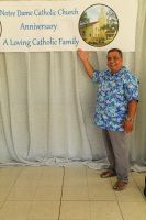 Woman points to Notre Dame Catholic Church anniversary banner beside a gray curtain backdrop.