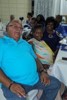 Man in a turquoise shirt seated at a banquet table beside a woman in a colorful dress at a gathering
